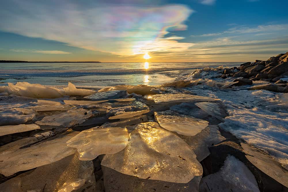 Frozen shoreline with ice and rocks at sunset in winter.