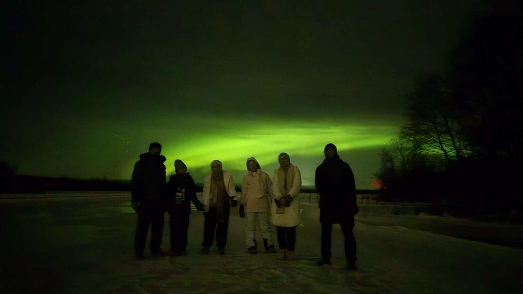Group of people viewing the Northern Lights at night in a scenic outdoor location.