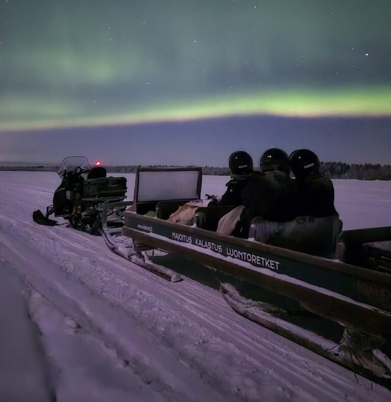 Snowmobile riding under the Northern Lights in Lapland at night.