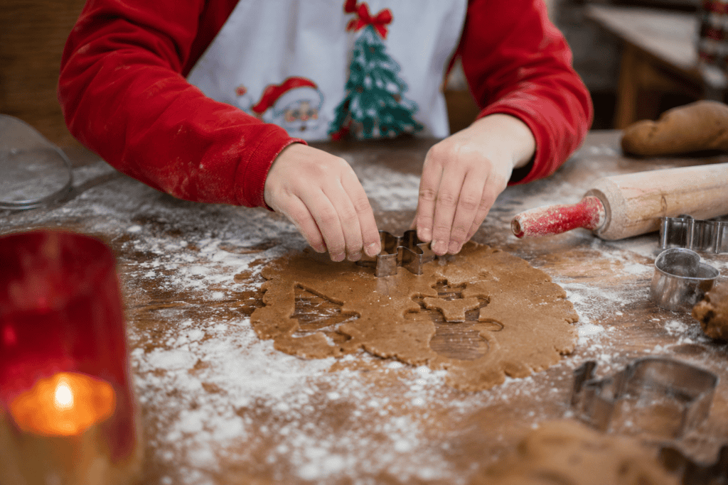 Child decorating holiday cookies with Christmas-themed shapes on dough.
