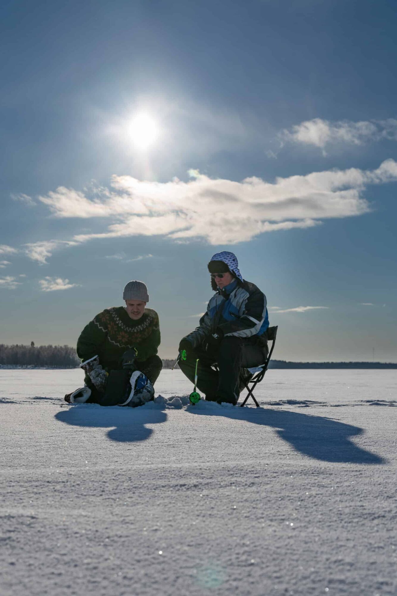Family ice fishing on a frozen lake under sunny sky at Aurora Sea Resort.